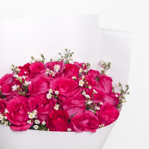 A bouquet of vibrant pink roses with small white flowers, wrapped in white paper.