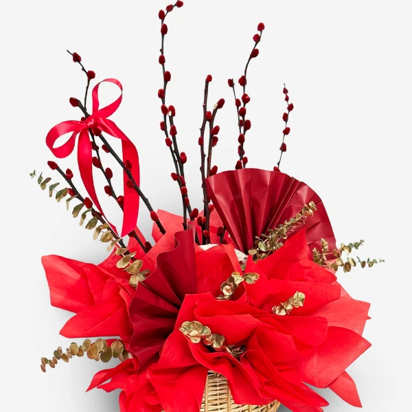 Red pussy willow branches, red fans, and gold eucalyptus leaves in a woven basket.