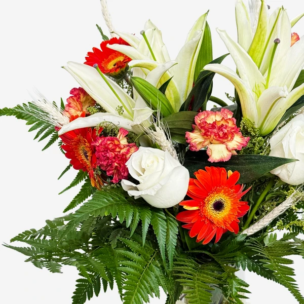 A bright floral arrangement of white lilies, red gerbera daisies, red carnations, and white roses with green ferns.