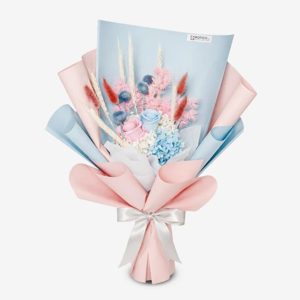 Bouquet of pink and blue preserved flowers with dried wheat and foliage, wrapped in light blue and pink paper, tied with a white ribbon.