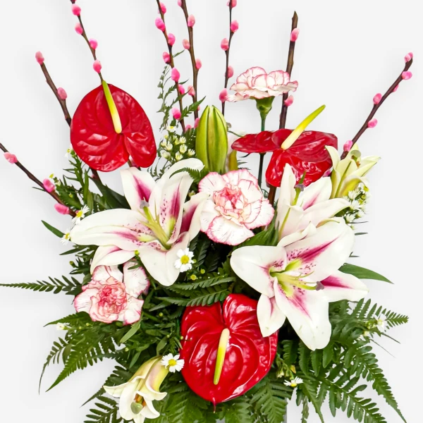 A vibrant floral arrangement of red anthurium lilies, white lilies, pink carnations, and pussy willow branches against a white background.