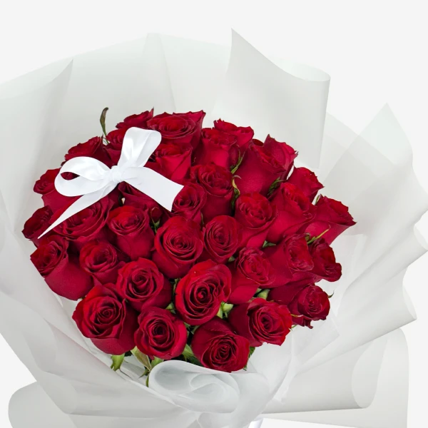 A lush bouquet of 30 deep red roses tied with a white ribbon, presented in white paper wrapping.