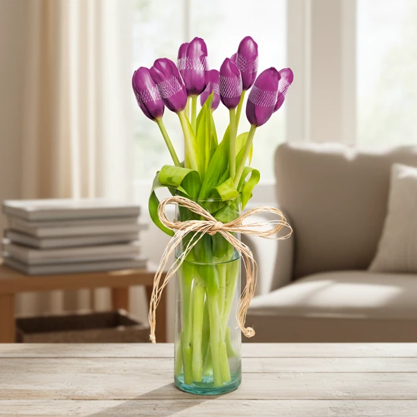 Violet tulips with a raffia bow in a clear glass vase on a wooden table.
