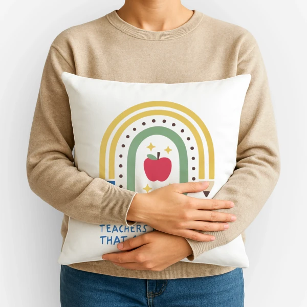 Person holding a pillow with a rainbow and apple design, featuring text about teachers.