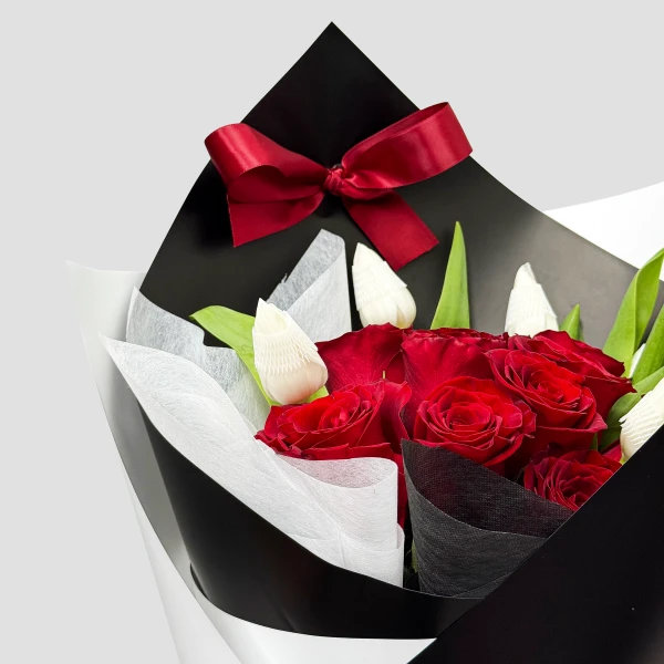 A bouquet of red roses and white tulips wrapped in black and white paper, tied with a red ribbon.