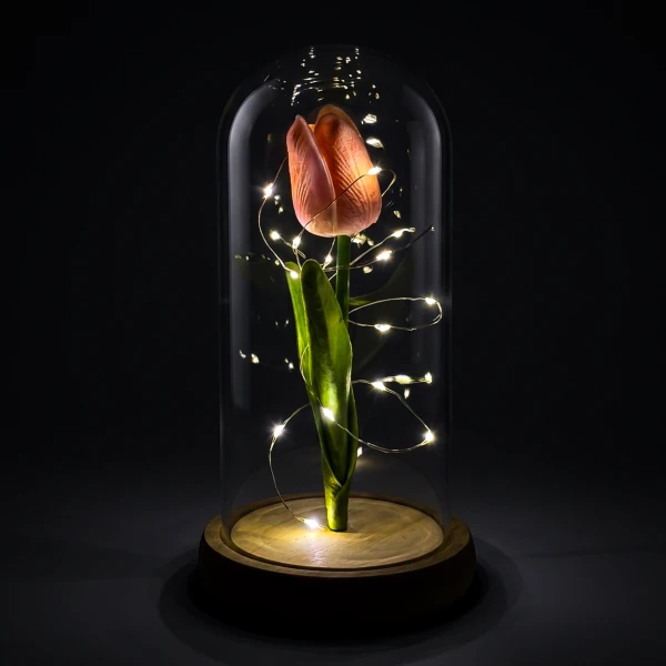 A pink tulip with fairy lights under a glass dome on a wooden base.
