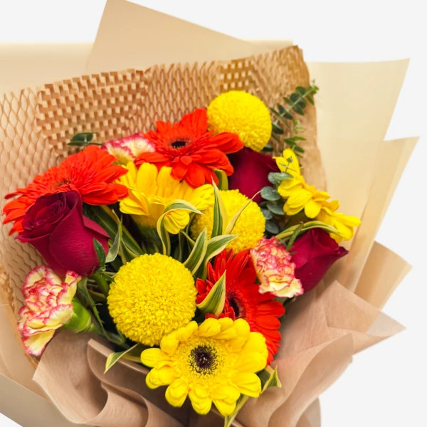 A bright bouquet of red, orange, and yellow gerbera daisies, roses, and chrysanthemums.