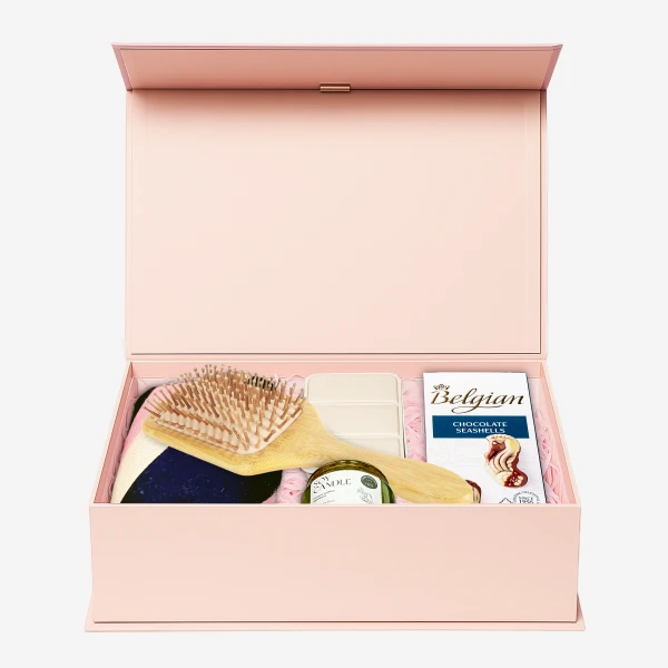 Pink gift box with hairbrush, candle, soap, and chocolate.