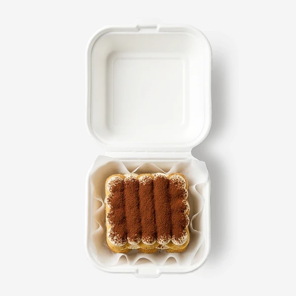 Square tiramisu in a white take-out box, sprinkled with cocoa powder.