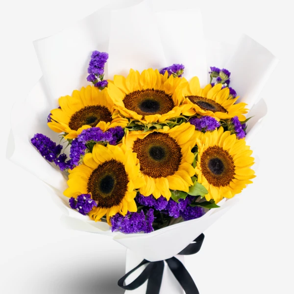 Bouquet of bright yellow sunflowers with purple filler flowers, wrapped in white paper and tied with a black ribbon.