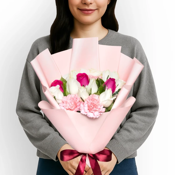 Woman holding a bouquet of white and pink roses and pink carnations, wrapped in pink paper and tied with a burgundy bow.