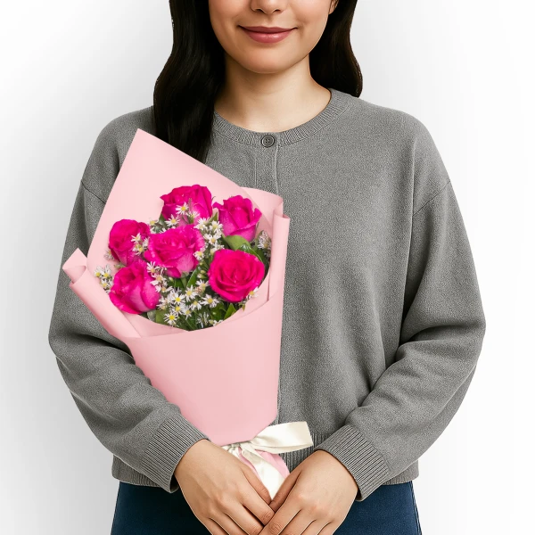 Person holding a bouquet of 6 bright pink roses wrapped in pink paper, tied with a cream ribbon.