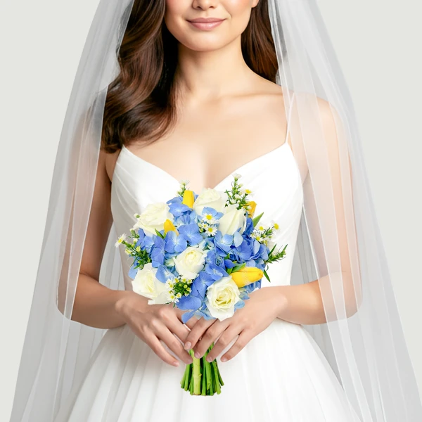 Bride in a white dress holding a bouquet of white roses, blue hydrangeas, and yellow tulips under a veil.