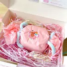 Candle set in a gift box with pink tissue paper and shredded filler, featuring a pink wrapped candle with a bear sticker.