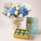Bouquet of blue hydrangeas & white roses, a card, and macarons in a gift box.