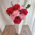 Pink and red carnations in a white vase on a wooden table.