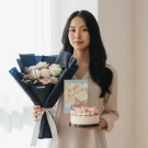 Woman holding a birthday bouquet, cake, and card.
