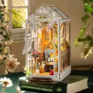 A miniature wooden greenhouse book nook with plants, furniture, and flowers, sitting on a book.