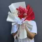 A dried flower bouquet with red and white blooms, wrapped in white and red paper with a pink ribbon.