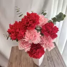 Pink and red carnations in a white vase with eucalyptus sprigs, on a wooden surface.