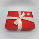 Red gift box with a white ribbon tied in a bow, featuring gold text and hearts.