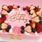 Pink strawberry cake with 'Happy Birthday' topper and fresh berries.