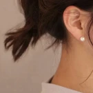 Close-up of a woman's ear with a single round pearl stud earring.