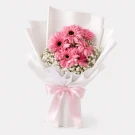 Pink gerbera daisies and baby's breath in white paper wrap, tied with a pink ribbon.
