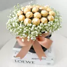 Ferrero Rocher chocolates and white gypsophila in a black box tied with a peach ribbon, presented on books.