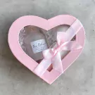 Pink heart-shaped box with bath bomb and rose bath salts, tied with a pink ribbon.