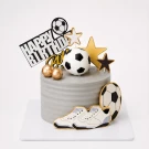 Gray cake with football decorations, stars, gold balls, and sneakers.