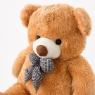 Giant teddy bear, brown, fluffy, wearing a checkered bow tie, against a white background.