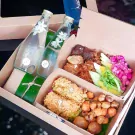 Khao Chae box set for 2 people, featuring two glass bottles of jasmine water, fried items, shredded pork, and colorful garnishes.