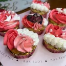 Six Valentine's Day cupcakes topped with pink and white frosting and decorative pearls, arranged on a pink tray.
