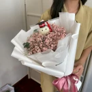 Graduation bouquet with a knitted figurine wearing a cap, surrounded by pink baby's breath and green leaves, tied with a pink ribbon.