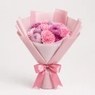 Pink and purple carnations and mums arranged in a bouquet, wrapped in pale pink paper with a satin bow.