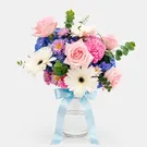 Pink roses, white gerbera, blue hydrangea, and pink carnations in a vase tied with a blue ribbon.