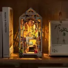 Miniature greenhouse book nook with chair, plants, and lights on a shelf.