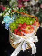 Fruit basket with grapes, strawberries, apples, and blue and white flowers in a woven basket.