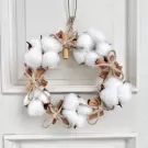 Wreath of cotton balls and cinnamon sticks tied with twine on a white door.