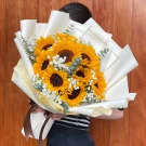 A bouquet of ten sunflowers, gypsophila, and eucalyptus, wrapped in cream paper and tied with a brown ribbon.
