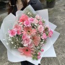 Pink gerbera daisies and carnations with baby's breath in a white bouquet wrapper.