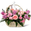 A wicker basket overflowing with pink, purple, and peach roses and carnations, tied with a white ribbon.