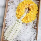 Yellow and white flower garland with a diamond accent, presented in a gift box lined with shredded paper.