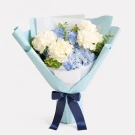 A bouquet of white carnations and blue hydrangeas wrapped in pale blue paper and tied with a navy ribbon.