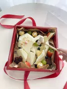 Red box with a white chocolate heart cake, fruits, chocolates, and a hammer.