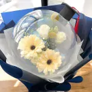 Graduation bouquet with flowers in a clear balloon, topped with a black graduation cap and red tassel.