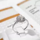 Close-up of an oval-cut moissanite diamond ring with a halo setting on a white display.