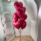 A bouquet of 7 red heart-shaped balloons tied with ribbons.
