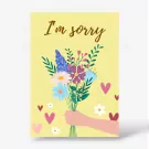 A yellow card with "I'm sorry" written in gold script above a bouquet of colorful flowers held by a hand.